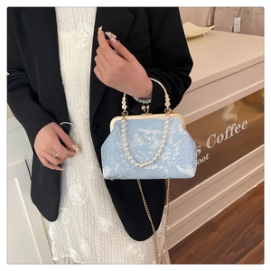 Light blue kiss-lock bag with pearl handle and gold chain strap in a lifestyle setting