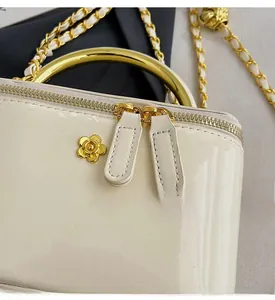 Close-up of smooth dual zippers and golden camellia logo on beige patent leather bag