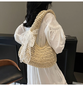Detail of hand-woven beige straw hobo bag featuring a large white lace bow on the shoulder strap