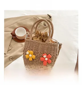 Detail of woven straw bucket bag featuring plush flowers and drawstring closure