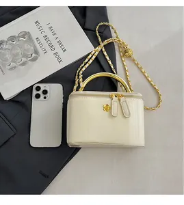 Mini cream box bag with gold handle and chain strap shown next to a smartphone