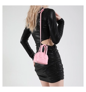 Mini sac à main rose verni en forme de coquille avec bandoulière porté par un mannequin
