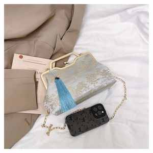Detail of silver brocade evening bag with gold patterns and blue tassel on white cloth