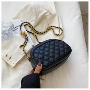 Detail of black quilted leather chain bag with gold metal ball on a white blazer