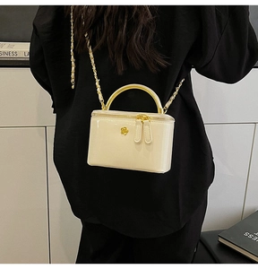 Detail of cream white leather mini bag with gold metal handle and floral charm detail