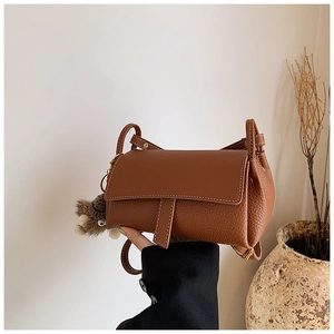 Détail du sac bandoulière en cuir marron grainé avec surpiqûres blanches et pendentif peluche