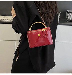 Detail of red patent leather handbag with gold curved handle and flower hardware