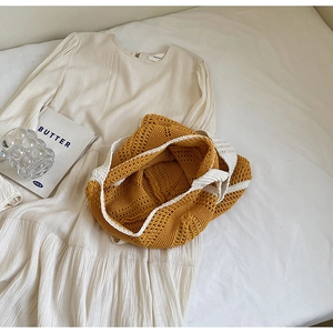 Detail view of ginger yellow hollow knit tote bag and beige pleated textured dress