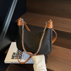 Minimalist black crescent bag with brown leather trim and chain strap on a wooden steps background