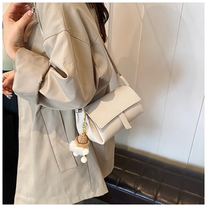 Gros plan d'un sac bandoulière beige en cuir grainé avec un charm pompon et chapeau tricoté