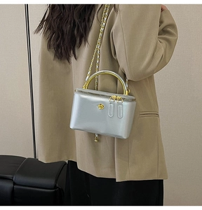 Detail of silver metallic handbag with gold top handles and chain strap worn by model