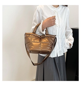 Detail of metallic bronze quilted nylon puffer bag featuring horizontal stitching and handles