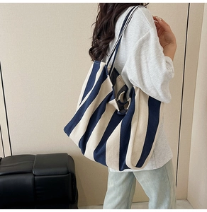 Detailed view of striped canvas tote bag worn by a model on a shoulder strap
