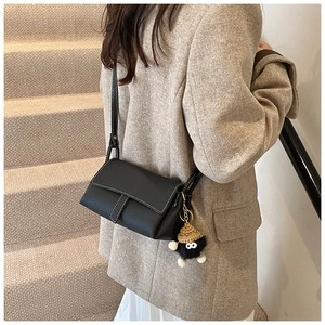 Détail du sac carré en cuir noir avec surpiqûres blanches et charme de monstre en peluche