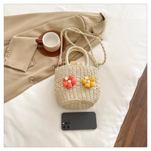 Detail of woven straw bucket bag with 3D floral accents and sturdy carry handles