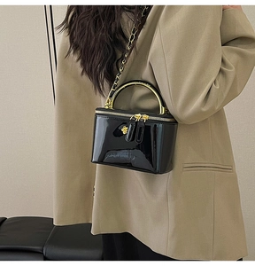 Détail du sac boîte en cuir verni noir brillant avec poignée dorée et curseurs floraux