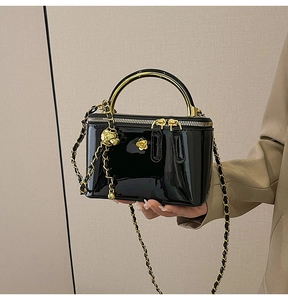 Détail du sac en cuir verni noir avec poignée anneau dorée et décoration de camélia