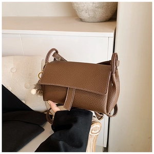 Détail du sac à bandoulière en cuir grainé marron foncé avec surpiqûres blanches et pompon