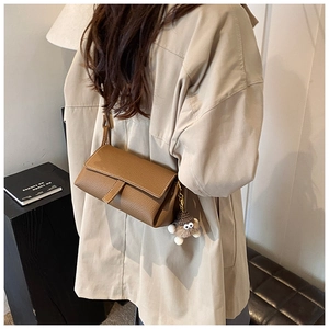 Gros plan sur un sac bandoulière en cuir marron avec un porte-clé en peluche grise