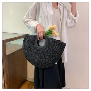 Close-up of a black woven straw handbag featuring a unique semi-circular shape and textures