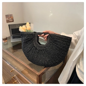 Macro shot of black hand-woven straw handbag featuring a unique semi-circular cutout handle