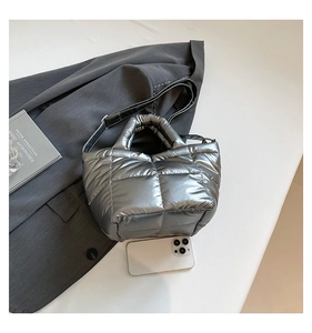 Detail of silver puffer tote bag with quilted texture and adjustable black strap on gray blazer