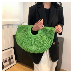 Detail of a bright green woven straw handbag featuring a unique half-moon clamshell design