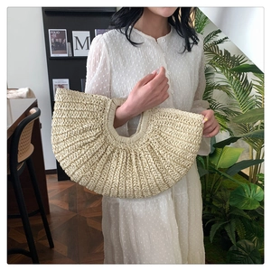 Detail of a beige semi-circular woven straw handbag with pleated texture for summer