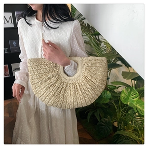Detail of a cream woven straw handbag with a bohemian style held by a model in a white dress