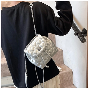 Close-up of silver heart-quilted crossbody bag with metallic chain strap and drawstring