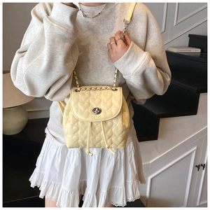 Detail of light yellow heart-quilted mini backpack with silver chain strap and metal lock