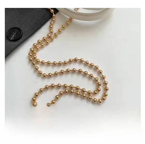 Detail of golden polished bead chain strap and white leather connector on mini shell bag