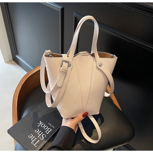 Detail view of cream bucket bag with V-shaped stitching and adjustable strap on a chair