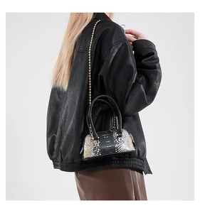 Detail of snake pattern mini shell bag with gold chain strap shown on a female model