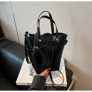 Close-up of black glossy leather bucket bag with silver hardware on a white book decor