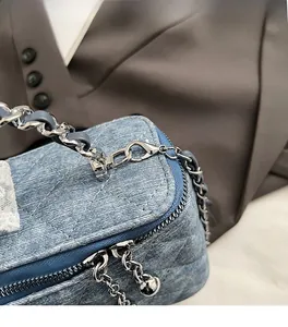 Detail shot of silver metal lobster clasp and premium blue denim fabric on the handbag