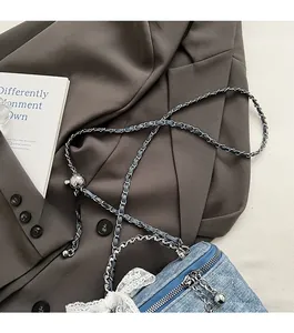 Detail of light blue denim crossbody bag featuring a large lace bow and silver chain strap
