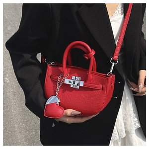 Dettaglio borsa in pelle rossa con fibbia in metallo e ciondolo a cuore su una modella
