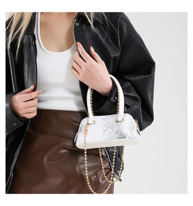 Detailed close-up of a mini white snakeskin shell bag with gold chain strap on model