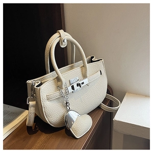 Dettaglio della borsa in pelle beige con trama litchi, chiusura e ciondolo a cuore