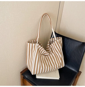 Close-up of a striped canvas tote bag with long straps and front pocket on a chair