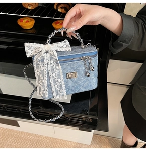 Blue denim box bag with quilted pattern, white lace bow, and silver chain handle detail