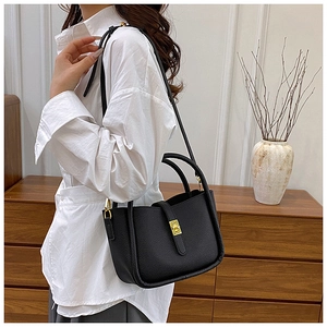 Litchi texture black leather handbag detail with elegant gold buckle on white shirt model