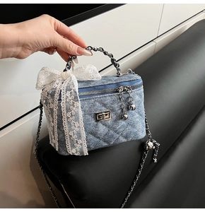 Detail of denim box bag featuring white lace bow and silver chain strap for women