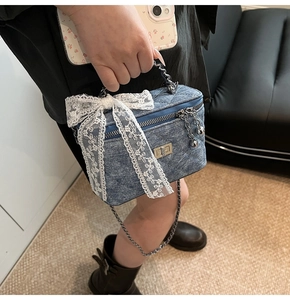 Detail of blue denim quilted box bag featuring white lace bow and silver chain strap