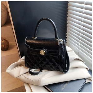 Détail d'un sac à main noir matelassé avec fermoir doré posé sur une veste beige