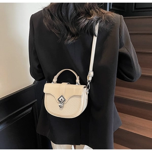 Sac selle beige tendance avec texture tissée et fermoir en métal porté par un mannequin