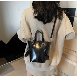 Crossbody view of black glossy bucket bag with dual handles and slender strap