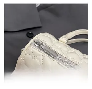 Détail de la fermeture éclair argentée et du motif de cœur matelassé sur le sac crème