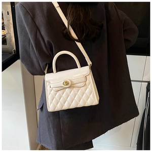 Détail d'un sac à bandoulière matelassé blanc avec fermoir tournant doré et chaîne